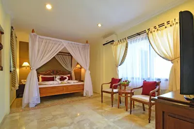 a bedroom with a canopy bed and two chairs at Puri Dewa Bharata Hotel & Villas in Legian
