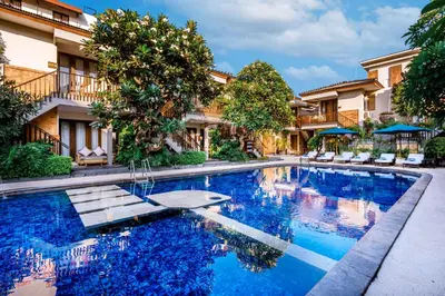 a swimming pool in front of a building with trees at Rama Garden Hotel Bali in Legian