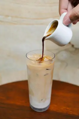 a person pouring a spoon into a glass of coffee at Wina Holiday Villa Kuta Bali in Kuta