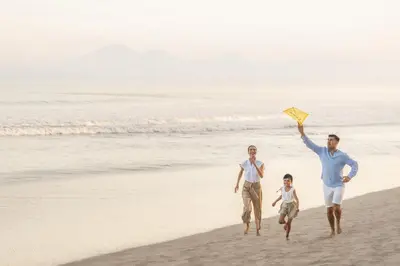 a family running on the beach with a kite at InterContinental Bali Resort by IHG in Jimbaran