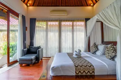 a bedroom with a bed and a chair and windows at Bali Prime Villas Seminyak by Kanaya Hospitality in Seminyak