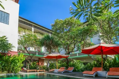a swimming pool with chairs and umbrellas next to a building at Capital O 1666 Grand Pudjawan Hotel Near Kuta Beach in Kuta