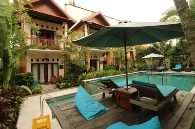a pool with chairs and an umbrella next to a house at Mina Pelasa Hotel in Legian