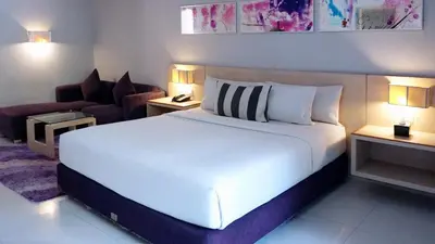 a bedroom with a large white bed and a couch at Conjioo Hotel Kuta Managed By MHM in Legian