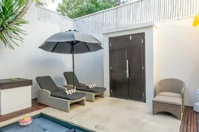 a patio with two chairs and an umbrella and a pool at The Town House in Seminyak