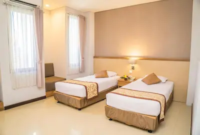 two beds in a hotel room with two windows at Hotel Puri Ayu in Denpasar