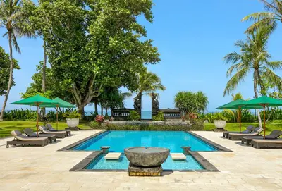 a swimming pool with a fountain and chairs and umbrellas at The Patra Bali Resort & Villas - CHSE Certified in Kuta
