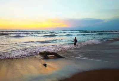 a man standing on the beach near the ocean at Dwiputra Guest House in Canggu