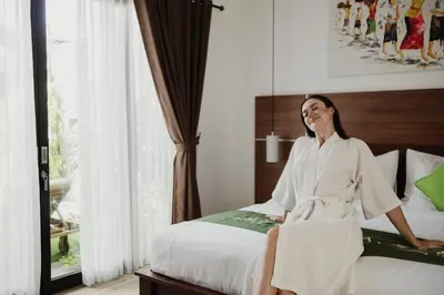a woman in a robe sitting on a bed at Gracia Bali Villas & Apartment Managed by Manara in Seminyak