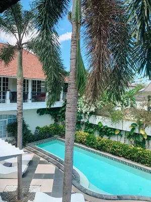 a swimming pool in front of a building with palm trees at Casa Artista By Kresna Hospitality in Seminyak