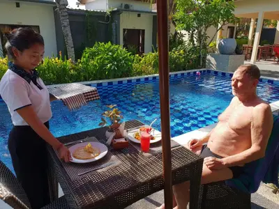 a woman standing next to a man sitting at a table near a pool at Palm Bamboo Hotel in Nusa Dua
