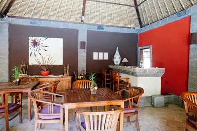 a restaurant with wooden tables and chairs and a red wall at Ellies Hotel in Nusa Dua