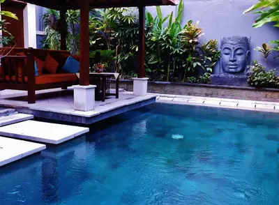 a swimming pool with a bench and a statue next to a house at Villa Kora in Seminyak