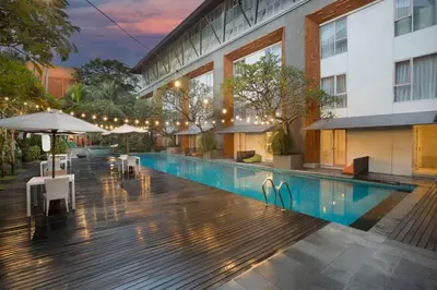 a hotel swimming pool with tables and umbrellas next to a building at HARRIS Hotel & Residences Sunset Road in Kuta