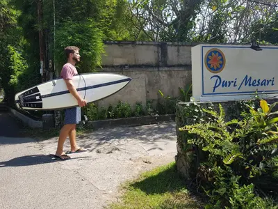 a man is holding a surfboard next to a sign at Puri Mesari Hotel in Sanur