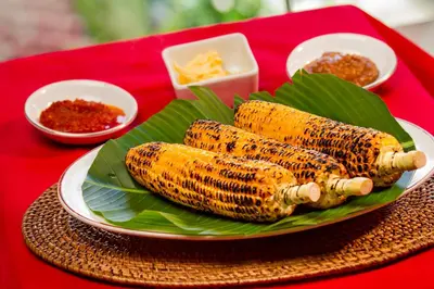 three grilled corn on a plate on a red table at Restu Bali Hotel in Legian