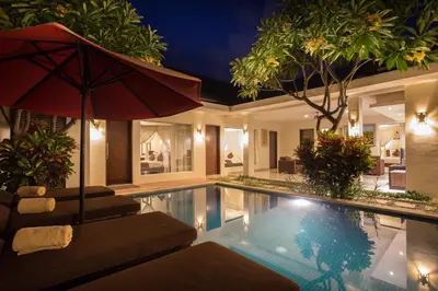 a swimming pool with an umbrella and chairs and a house at The Yubi Boutique Villas Seminyak in Seminyak
