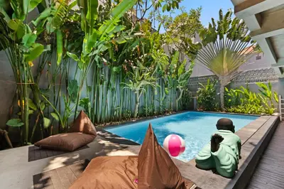 a swimming pool in a garden with a person sitting next to it at Balissimo Suites Seminyak by Betterplace in Seminyak