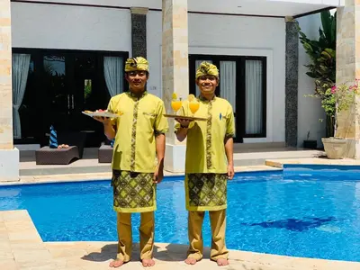 two men in yellow shirts holding drinks in front of a swimming pool at Casa Priya Seminyak in Kerobokan