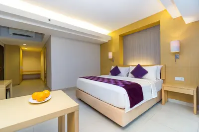 a hotel room with a large bed and a table at Quest Hotel Kuta by ASTON in Kuta