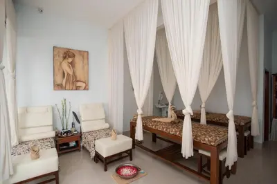 a bedroom with two beds with white curtains and chairs at Samsara Inn in Legian