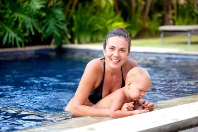 a woman holding a baby in a swimming pool at Amore Villas in Canggu