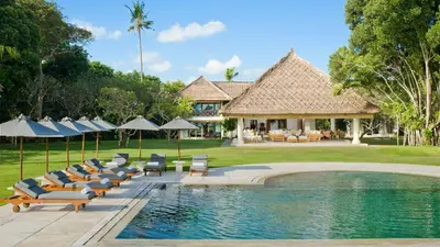 a pool with lounge chairs and umbrellas next to a house at Villa Atas Ombak in Seminyak