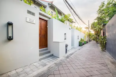 a narrow street with white buildings and a wooden door at Villa Neno in Seminyak