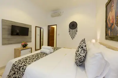 a white bedroom with a large white bed and a tv at Amerta Seminyak in Seminyak