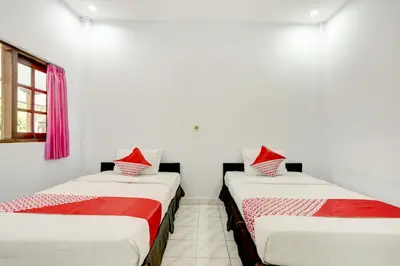 two twin beds in a room with a window at Hotel O Ratu in Denpasar