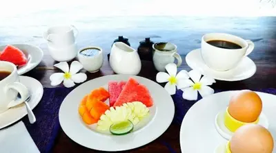 a table with a plate of fruit and cups of coffee at Tanjung Sari Inn in Nusa Dua
