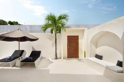 a patio with two chairs and an umbrella and a palm tree at The Grand Daha Luxury Villas in Seminyak