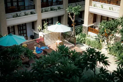a person sitting on a bench under an umbrella in front of a building at Fourteen Roses Beach Hotel in Legian