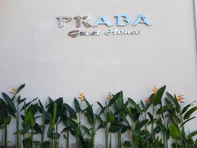 a sign for a guest house with a bunch of plants at Praba Guesthouse in Kuta