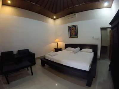 a bedroom with a bed with a lamp and a chair at Putu Guest House in Canggu