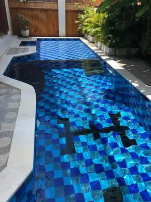 a swimming pool with blue tiles in a yard at Villa Chambertin in Seminyak