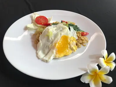 a white plate of food with an egg and pasta at Agus Beach Inn in Kuta