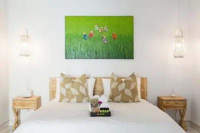 a bedroom with a white bed with a painting on the wall at Villa Orked 1 in Seminyak