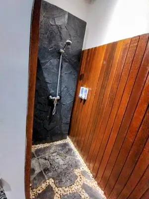 a shower in a bathroom with a stone wall at Villa Made West in Seminyak