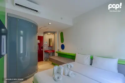 a bedroom with a white bed and a living room at POP! Hotel Kuta Beach in Kuta