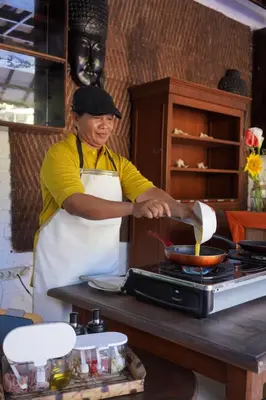 a woman in a kitchen preparing food on a stove at Sarinande Hotel in Seminyak