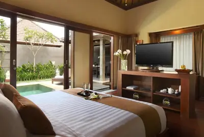 a bedroom with a tv and a bed and a pool at Nyuh Bali Villas in Seminyak