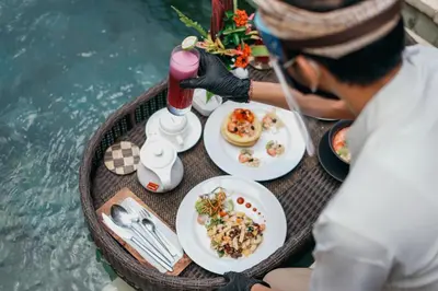 a man eating food on a table next to the water at Nyuh Bali Villas in Seminyak