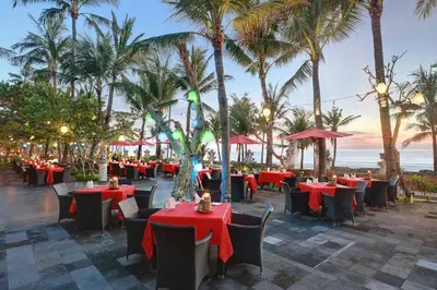 a restaurant with red tables and chairs and palm trees at Legian Beach Hotel in Legian