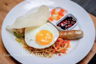 a plate of food with an egg and sausage and noodles at Grandmas Plus Hotel Legian in Legian