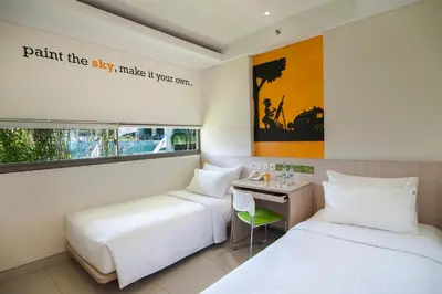 a hotel room with two beds and a desk at Grandmas Plus Hotel Legian in Legian