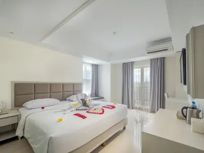 a white bedroom with a large bed with flowers on it at Alron Hotel Kuta in Kuta