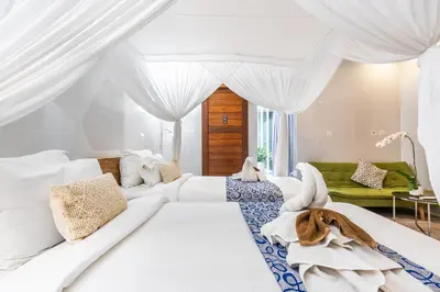 a white bedroom with white curtains and a white couch at Kubu Joglo Villa in Seminyak