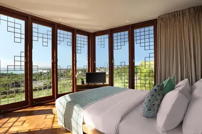 a bedroom with a bed and windows with a television at Dacolina House in Jimbaran
