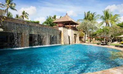 a swimming pool with a waterfall in front of a house at AYANA Villas Bali in Jimbaran
